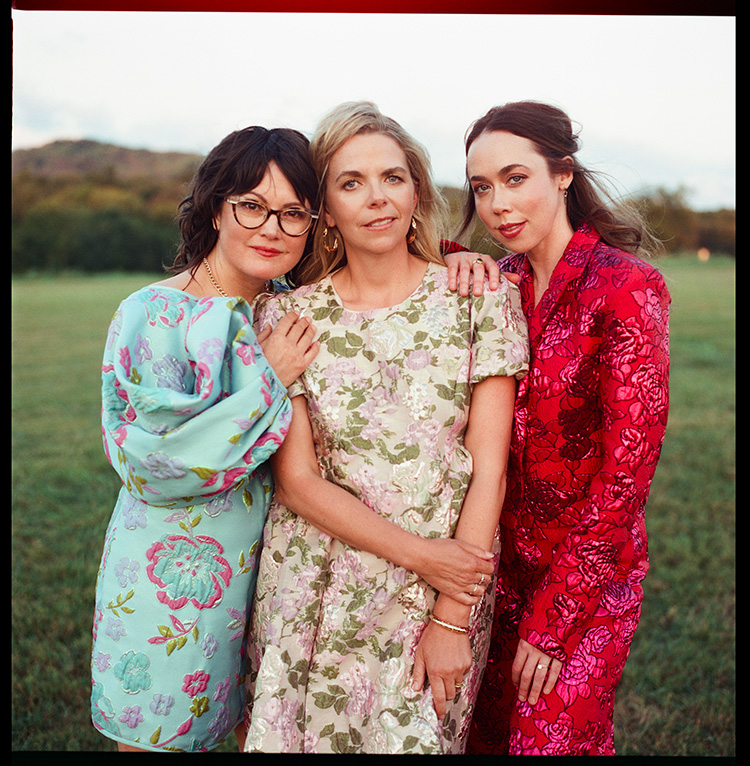 Three women posing for portrait in green field.